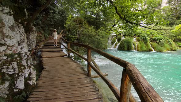 Happy traveler walking along a wooden bridge at Plitvice Lakes alt