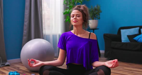 A Pretty Young Woman Dressed in Fitness Clothes Meditates While Sitting in Lotus Position on alt