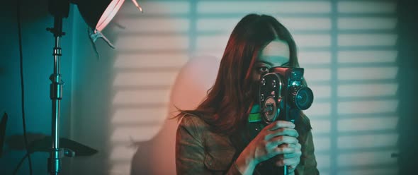 A woman in a video studio is holding a vintage video camera alt