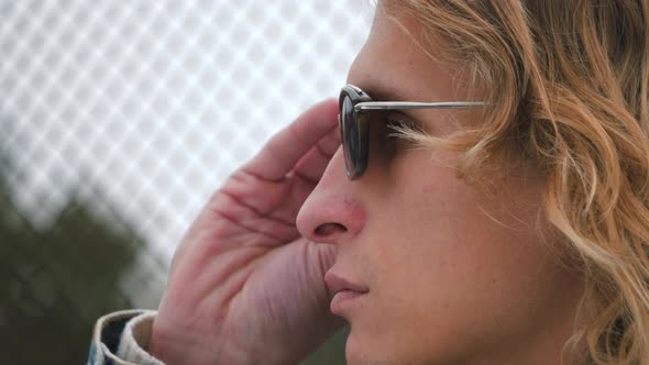 Side view of close up portrait. Stylish hipster man face with long blond hair put on sunglasses