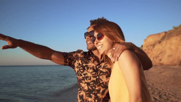 Young Beautiful Couple Speaking Smiling Laughing Walking at Seaside at Sunrise alt