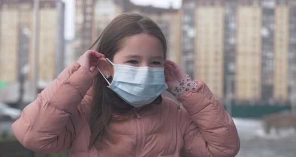 Coronavirus Protection. A Caucasian Girl Puts on a Medical Protective Mask Standing on a Street