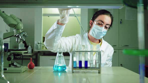 Scientist in Laboratory Doing Chemical Experiment with Blue Liquid in Test Tubes alt