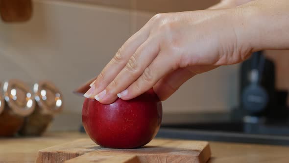 Woman cuts a ripe red apple with a knife.