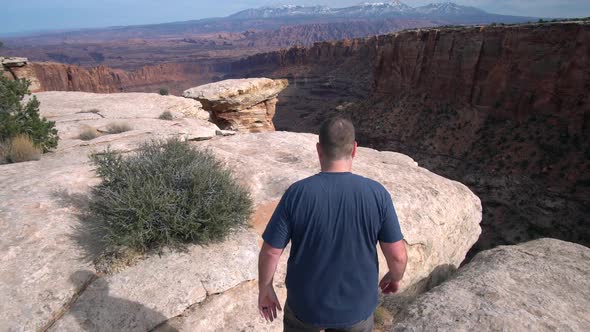 Following man walking towards the edge of a steep cliff alt