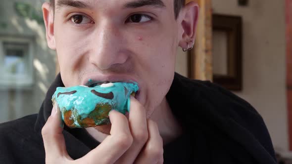 A Young Man Appetizingly Bites Off a Sweet Donut with Cream alt