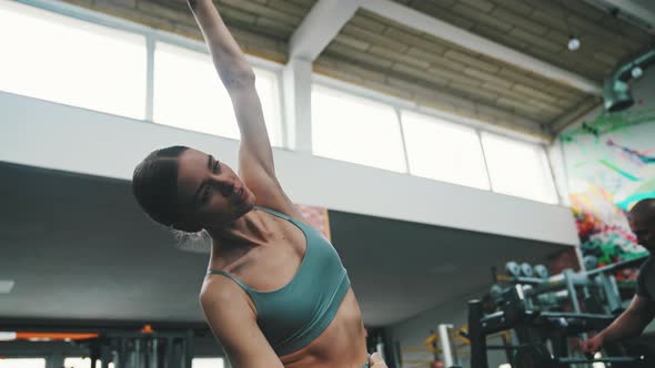 Attractive Caucasian Brunette in Gray Sports Bra Dynamically Stretching Her Arms at the Gym alt