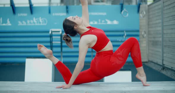Woman in Red Sports Costume Does Gymnastic Exercises on the Bench at Workout Playground Outdoors alt