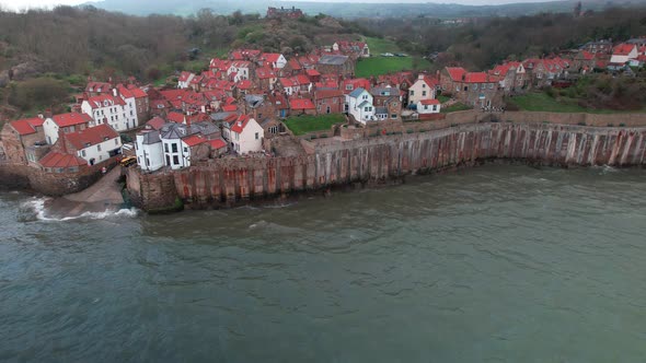 Aerial shot of houses situated just near the sea waves crashing in the rock. Rocky North Yorkshire C alt