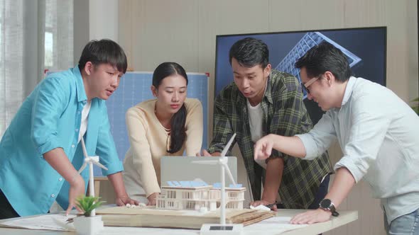 Asian Engineers Group With The Solar Panel House Model Discuss About  Work On A Laptop At The Office alt