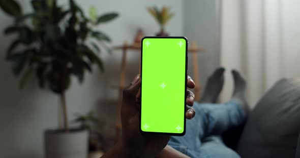 Close Up View of Man Holding Smartphone with Mock Up Screen While Lying on Sofa, Afro American Guy alt