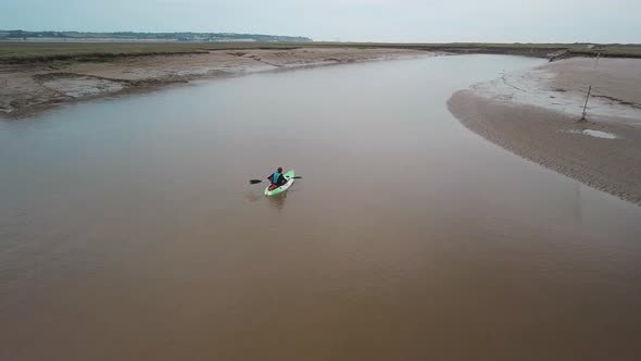 Man kayaking on meandering river, drone pans round kayaker. alt