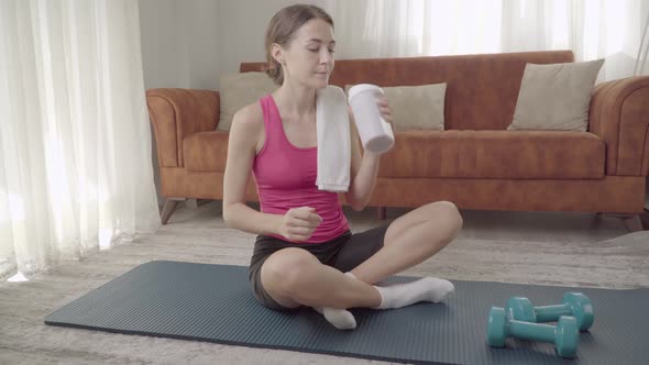 A Woman Shakes Her Shaker After Home Exercise and Drinks Protein