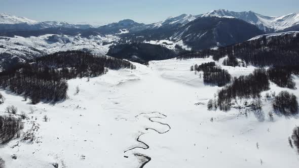 Amazing aerial view of a swirly river in the mountains during winter sunny day