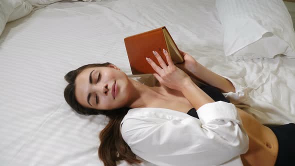 Beautiful Young Lady Relaxing at Home with a Writing Note in Hands While Lying on Large Bed alt