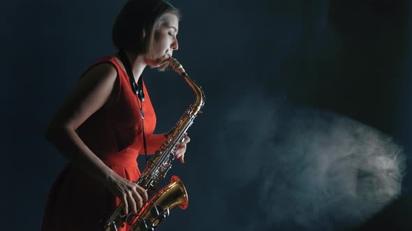 Beautiful Woman in Red Dress Playing a Melody on Saxophone. Smoky Dark Studio alt