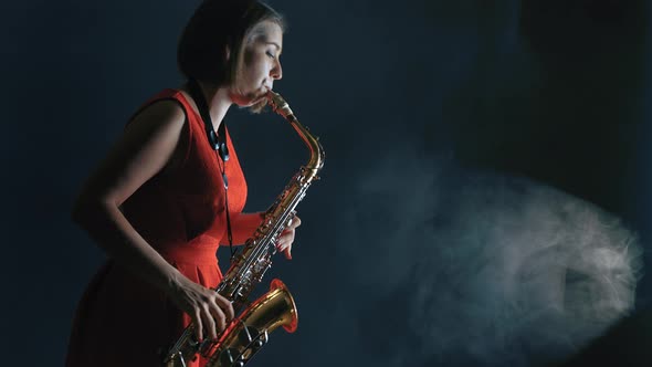 Beautiful Woman in Red Dress Playing a Melody on Saxophone. Smoky Dark Studio