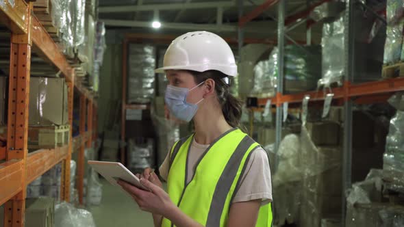 A Female Supervisor Wearing a Safety Vest Hard Hat and Face Mask During an Inspection at a Factory alt