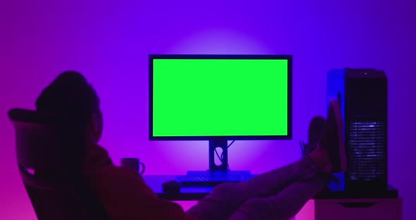 Young Man Freelancer Resting on a Chair Drinking Coffee and Looking at a Computer Monitor with a alt