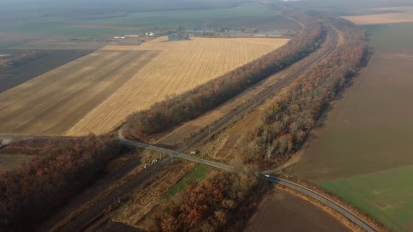 Panoramic View of Railroad Crossing Between Trees in Fields on Autumn Day alt