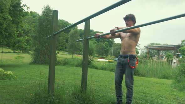 Fit topless youth performs straddle front lever on parallel bars outdoors at home gym in field alt