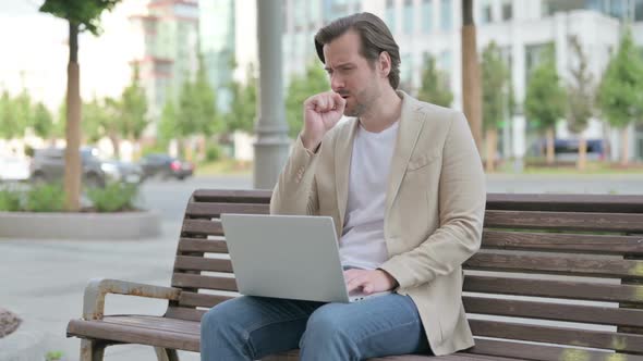 Coughing Young Man Using Laptop While Sitting on Bench alt