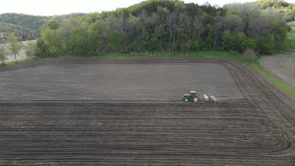 Farmer and his tractor fertilizing and seeding a section of farm. Cloudy sky overhead.