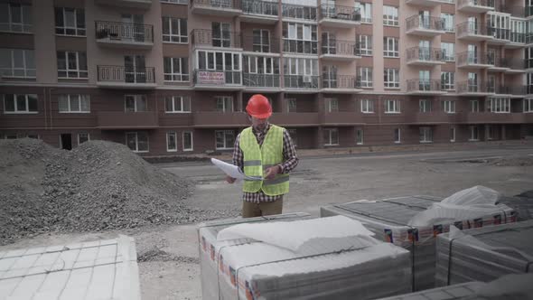 Male Builder Considers Brought Building Material at Construction Site Controls Materials alt