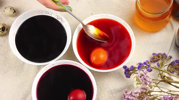 Caucasian Child Paints Easter Eggs with a Metal Spoon Dipped Into a White Bowl with Dye alt