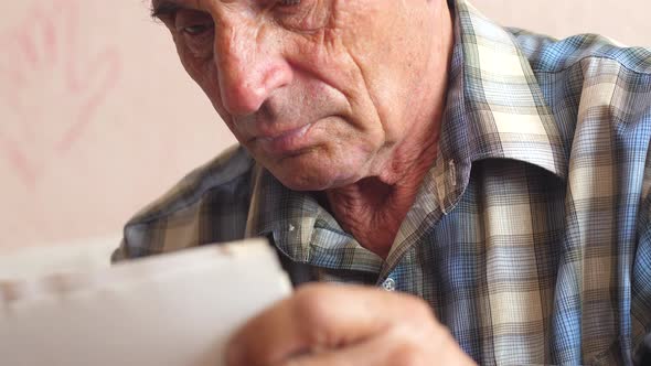  portrait of a caucasian pensioner 70-79 years old looking through photos holding in his hands.selec alt