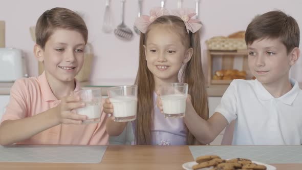 Three Happy Caucasian Children Clinking Glasses with Milk and Drinking Tasty Dairy Product, Portrait alt