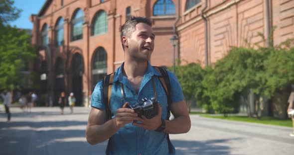 Medium Shot of Young Caucasian Tourist Man Smiling Happy Using Vintage Camera at City alt