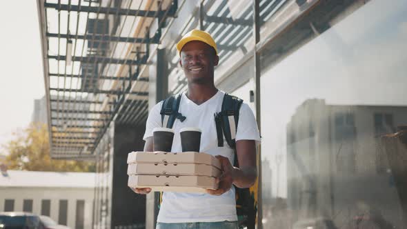 Black Male Courier with Cardboard Boxes Delivering Coffee Cups and Pizza to alt