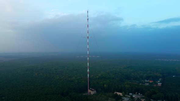 High TV tower on the edge of the city in the forest. Shooting from a drone.