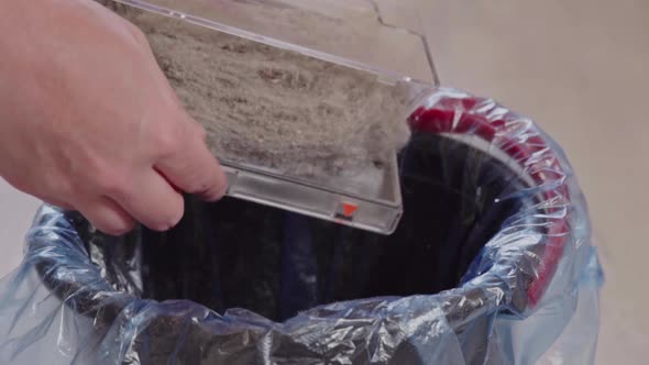 Hand removes the garbage from the dust container of the vacuum cleaner robot. Smart home alt