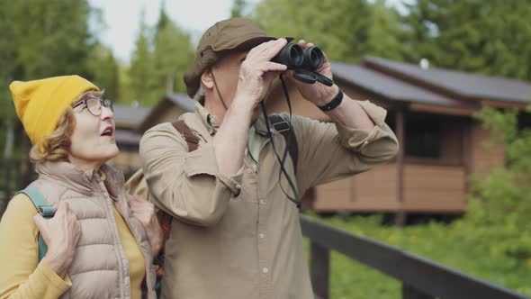 Senior Tourist Couple Using Binocular and Chatting during Hike alt