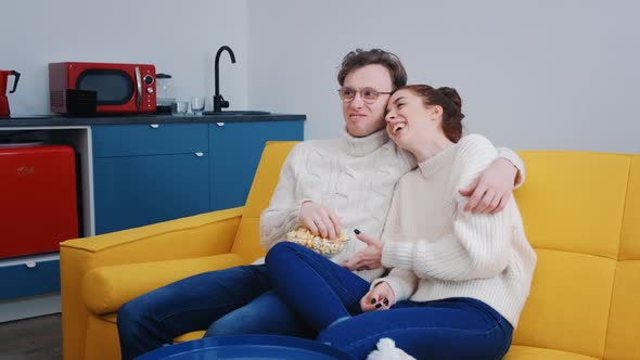a Young Beautiful Couple Spend Time Together at Home Watching TV and Laughing alt