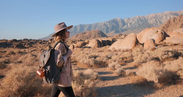 Smiling Fashionable Young Woman in Hat Walking By Desert Landscape at Sunrise alt