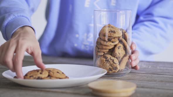 Homemade baking. Girl puts cookies from plate in glass jar chocolate chip cookies in glass jar with. alt