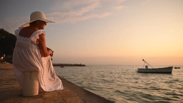 Senior Caucasian Woman Seating in Marina and Enjoying Sunset alt
