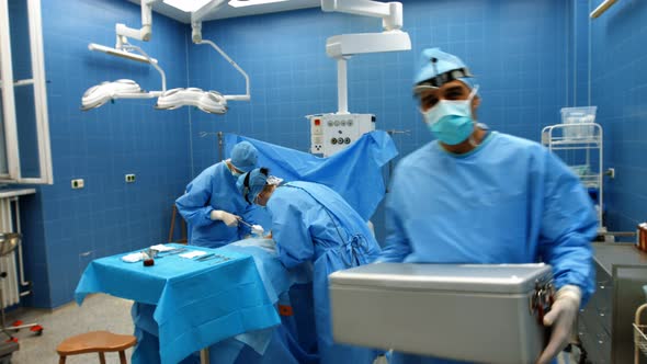 Portrait of surgeon holding ice box while colleagues performing operation alt