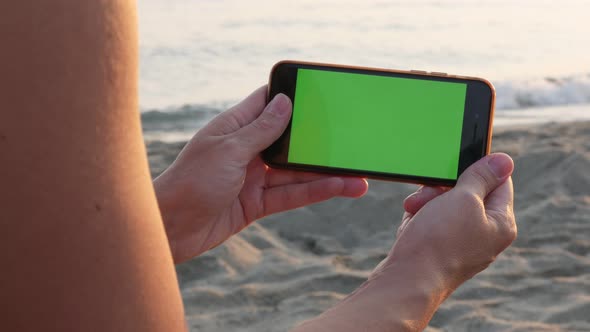 Green screen display smartphone in female hand by the sea 4K video