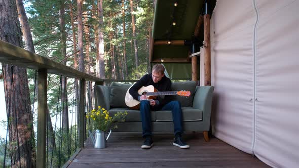 Man with Guitar Writes Song Outside Glamping Tent alt