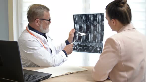 An Experienced Male Doctor Shows an X-ray Image and Explains the Diagnosis To a Young Female Patient alt