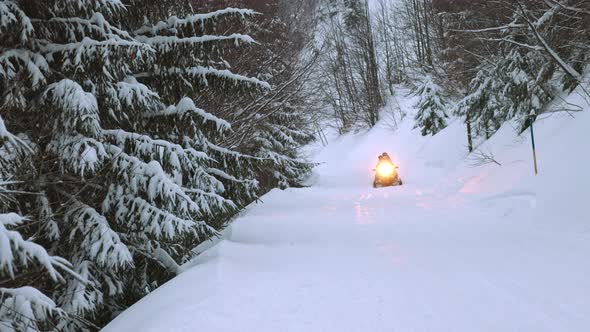 A Man on a Snowmobile Rides Along a Snowcovered Road Through the Forest Up a Hill in the Carpathian alt