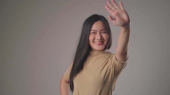 Happy asian woman waving her hand for greeting and looking at camera isolated over background.