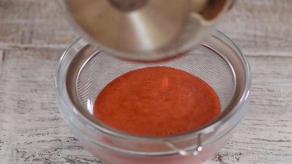 Professional cook hands prepares strawberry berry puree by rubbing through a sieve.
