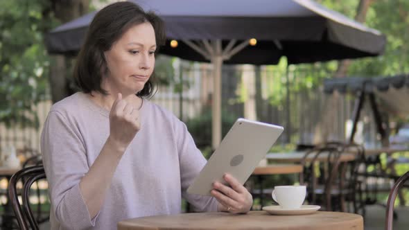 Upset Old Woman Reacting to Loss on Tablet in Outdoor Cafe alt