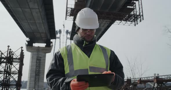Man Using Tablet on Bridge Construction Site alt
