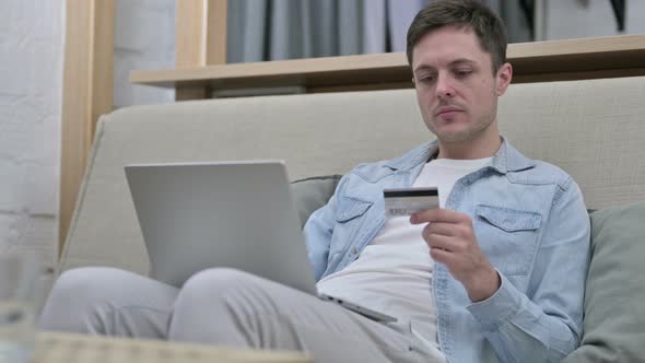 Young Man Making Online Payment on Laptop on Sofa  alt